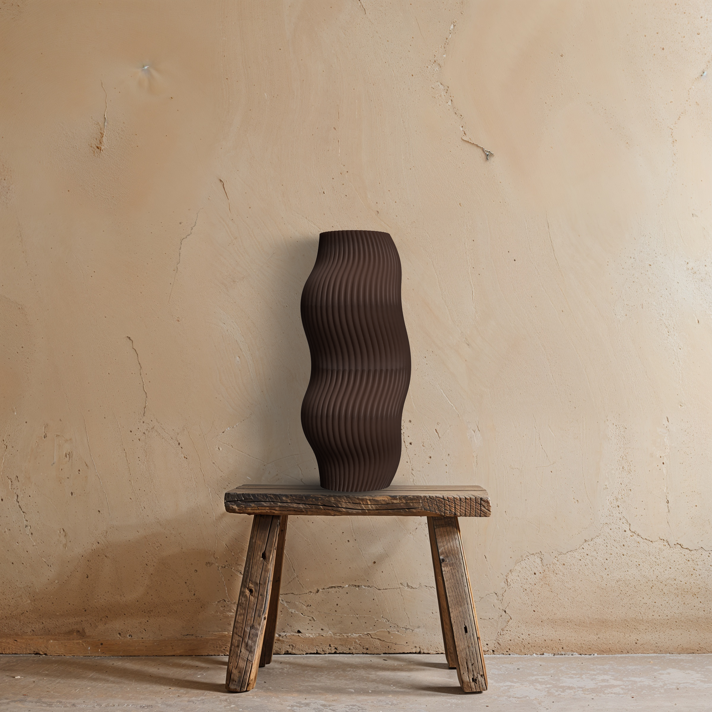 3D vaas Grazia in donkerbruin, gemaakt van gerecycled bioplastic, staat op een houten stoel tegen een zandkleurige muur.